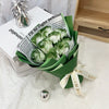 A bouquet of artificial green and white roses wrapped in dark green paper sits on a white surface.