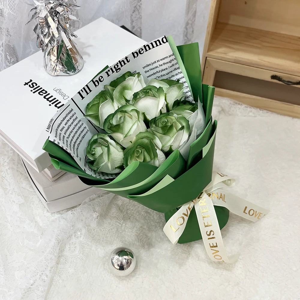 A bouquet of artificial green and white roses wrapped in dark green paper sits on a white surface.
