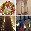 A festive wreath decorated with red ribbon and lights, a fireplace mantel display of string lights, and a garland of globe li