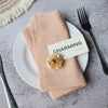 A stack of soft peach-colored handcrafted cotton napkins with a small floral decoration placed on a white plate.