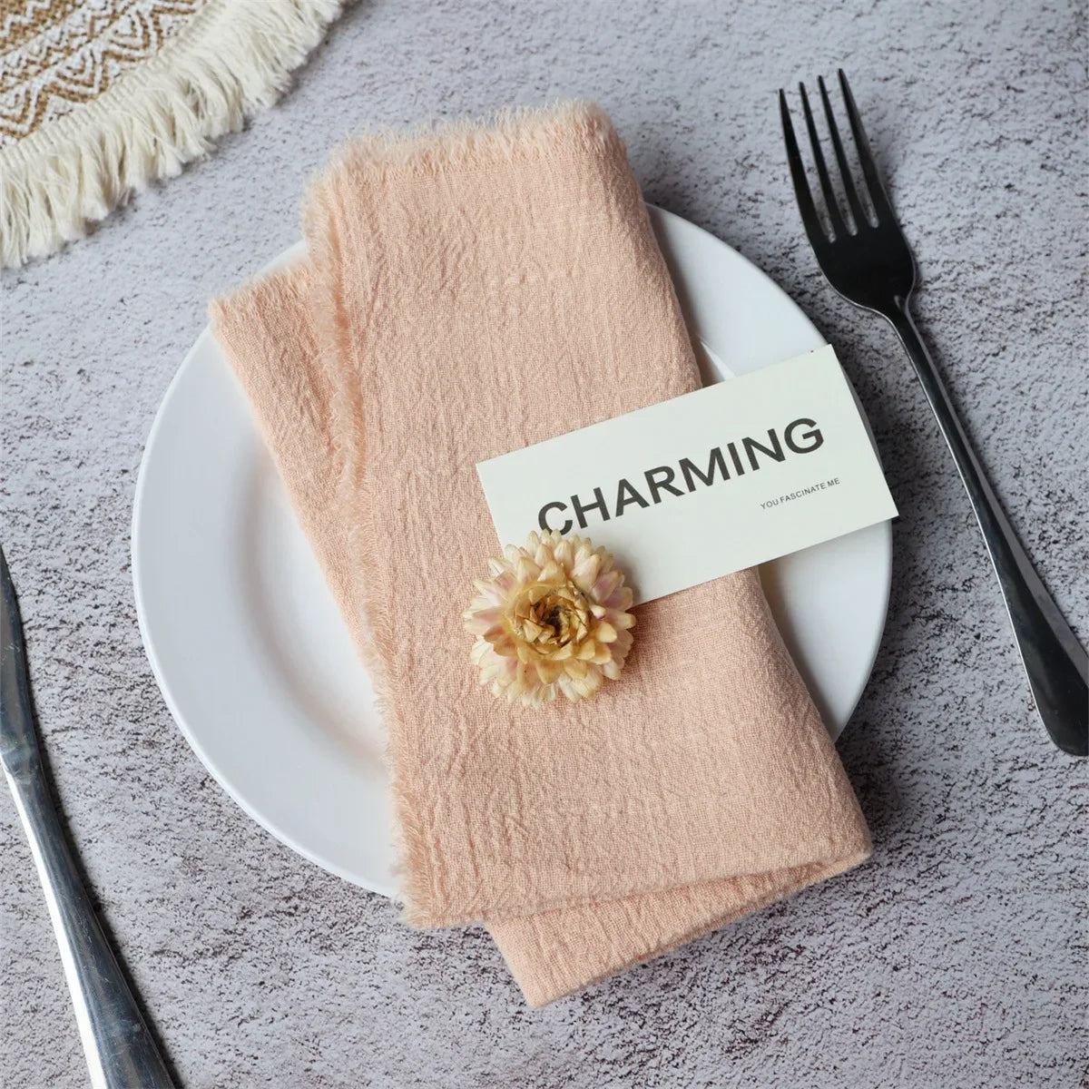 A stack of soft peach-colored handcrafted cotton napkins with a small floral decoration placed on a white plate.