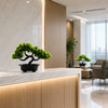 An artificial bonsai pine tree in a black pot displayed on a modern light-colored countertop.