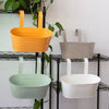 Three modern metal hanging planters in orange, gray, and white are displayed on a black wire rack.