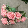A bouquet of pink roses and green foliage with small white filler flowers on a gray fabric background.