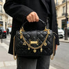 A woman holds a black quilted leather handbag with gold chain accessories on a city street.