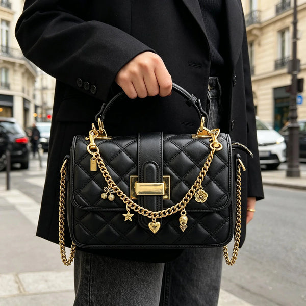 A woman holds a black quilted leather handbag with gold chain accessories on a city street.