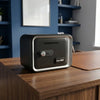 A black digital safe box with a silver trim sits on a wooden table.