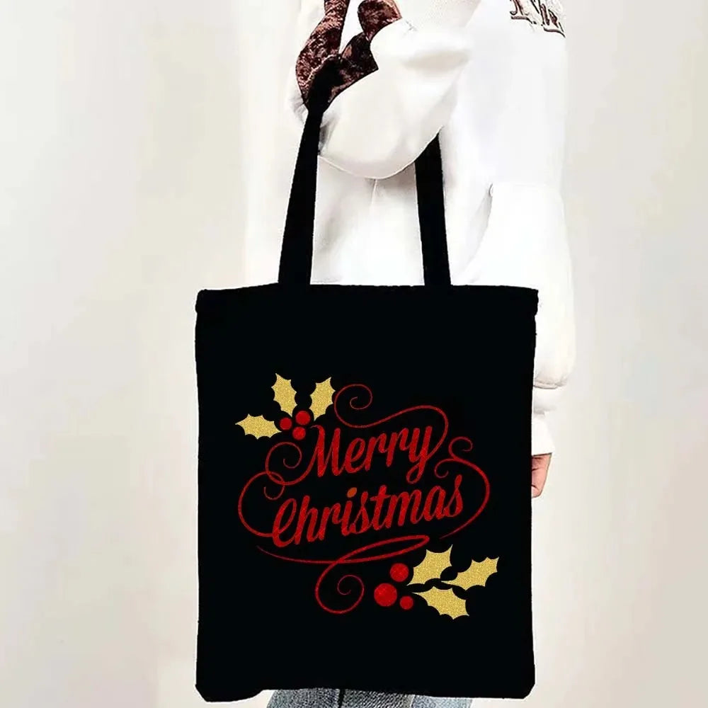 Black tote bag featuring a red script design of Merry Christmas with gold holly leaves