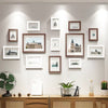 A collection of wooden picture frames displayed on a light gray wall, featuring various landscape and architectural prints.