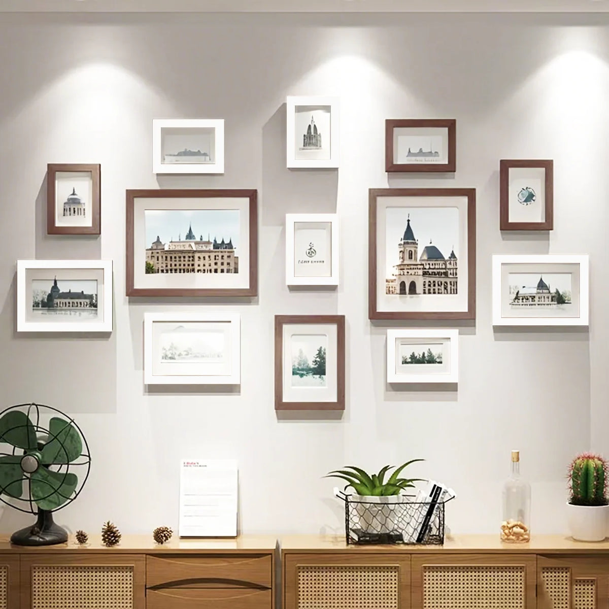 A collection of wooden picture frames displayed on a light gray wall, featuring various landscape and architectural prints.