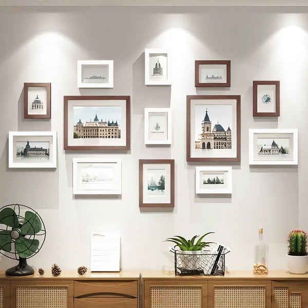 A collection of wooden picture frames displayed on a light gray wall, featuring various landscape and architectural prints.