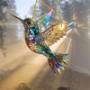A colorful acrylic hummingbird suncatcher ornament with iridescent wings hanging against a bright, backlit background.