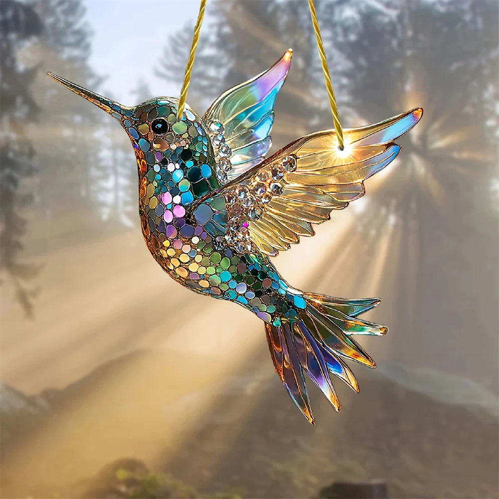 A colorful acrylic hummingbird suncatcher ornament with iridescent wings hanging against a bright, backlit background.