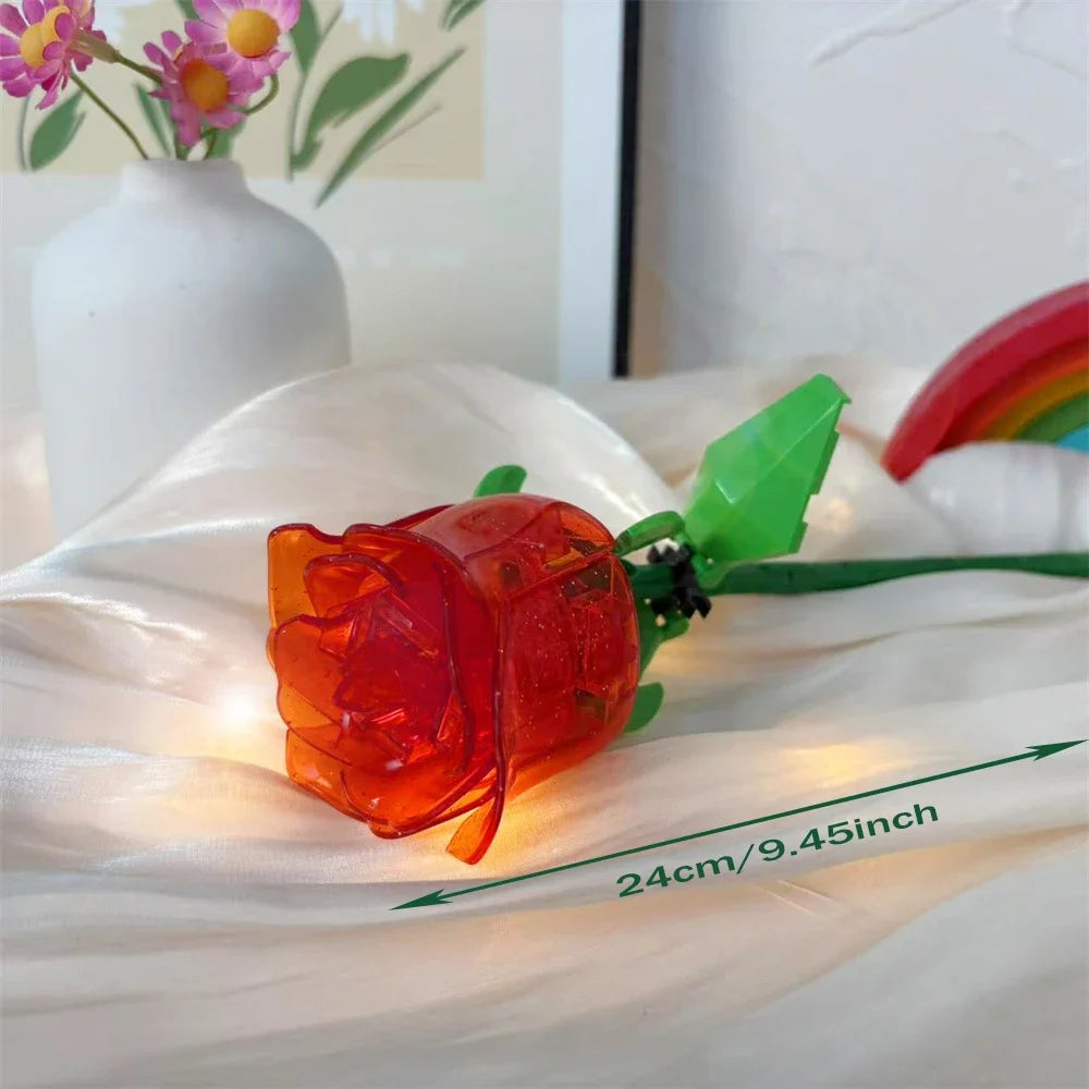 An orange glass rose flower building block with a green stem and leaves resting on white fabric.