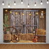 A rustic western backdrop featuring a weathered wooden barn door decorated with hay, a wooden wagon wheel, and antique leathe