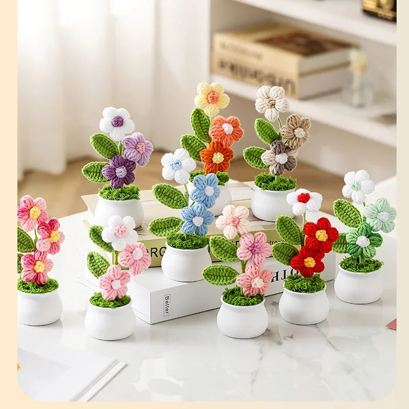 A collection of hand woven crochet flowers in various colors potted in white ceramic containers on a marble surface.