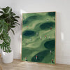 A framed canvas wall art painting depicting a green golf course with several small figures playing.