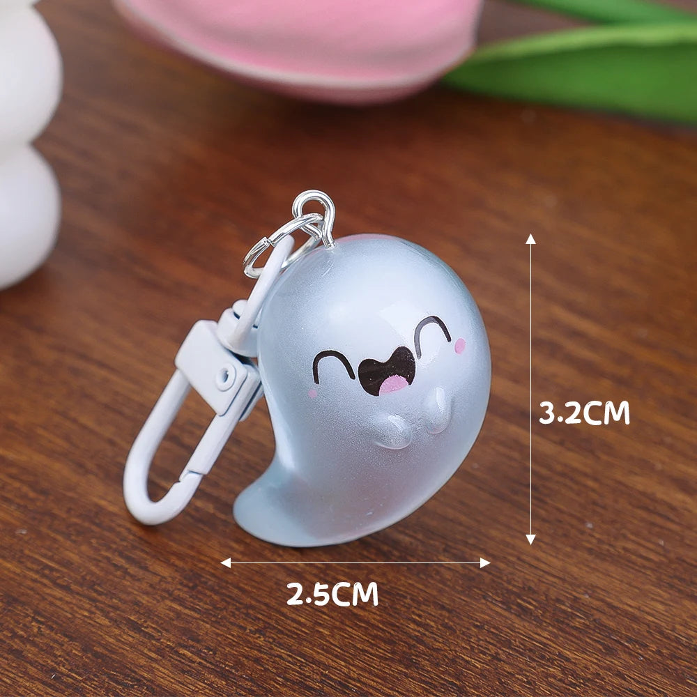 Silver glow-in-the-dark ghost keychain with a cute face, shown on a wooden surface.