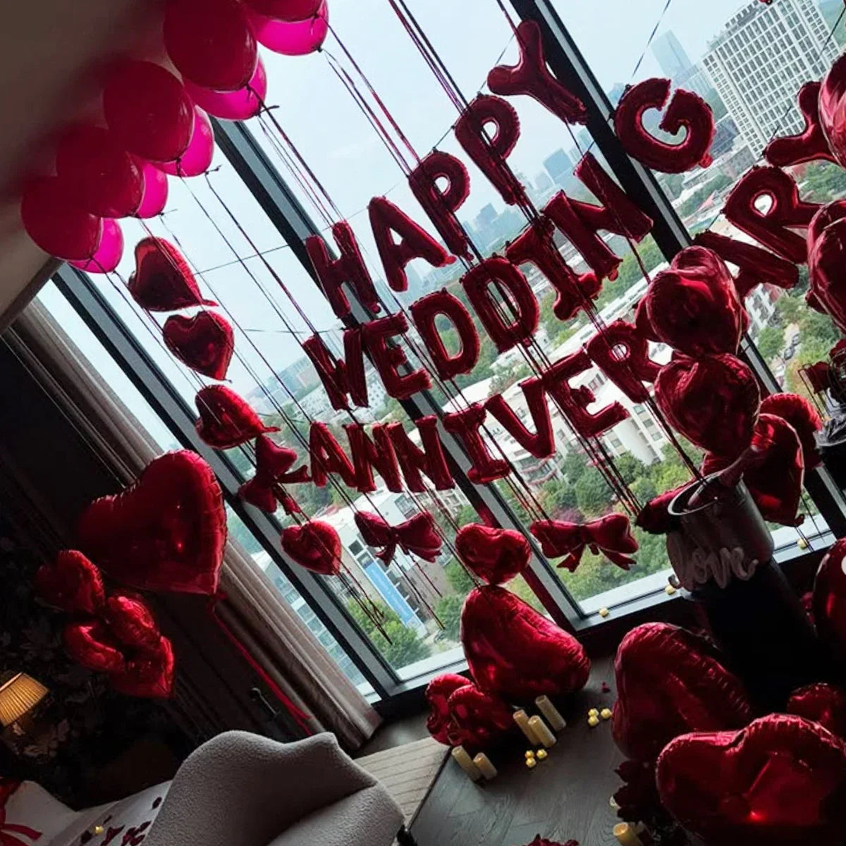 A display of red foil birthday balloons shaped like hearts with bows hanging in front of a window.