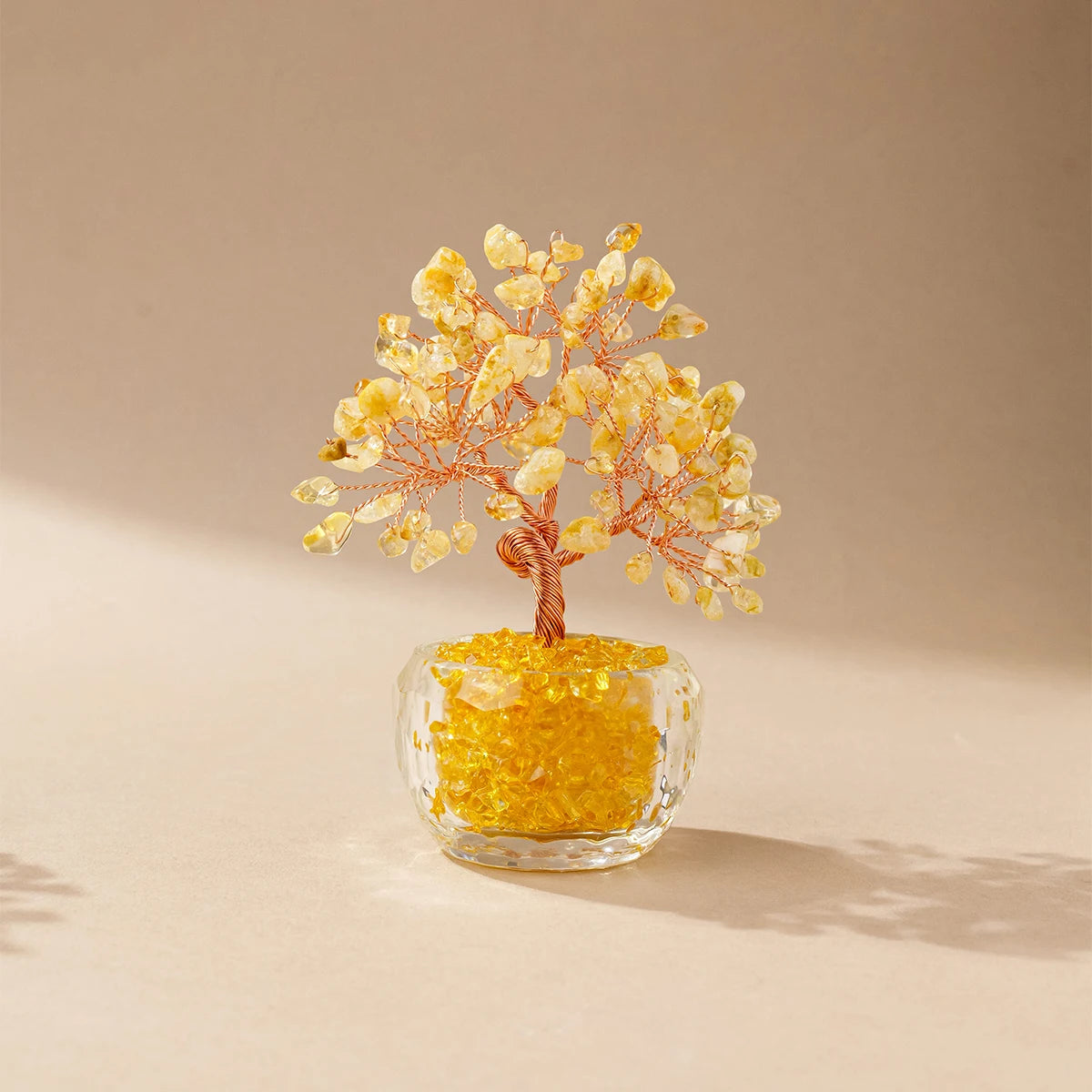 A natural crystal money tree ornament featuring golden yellow crystals on a thin wooden branch set in a clear glass base.