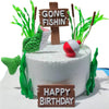 A white cake decorated with fishing theme elements including a fish, a wooden cross sign saying Gone Fishin', and a birthday 