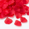 A pile of vibrant red silk rose petals scattered on a white surface.
