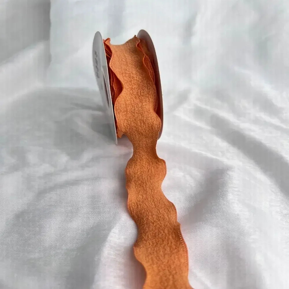 A close-up of a piece of orange felted yarn ribbon shaped like a fishtail, lying on white fabric.