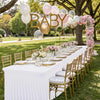 A long white table set for an outdoor event featuring gold chairs and balloons in a park setting.