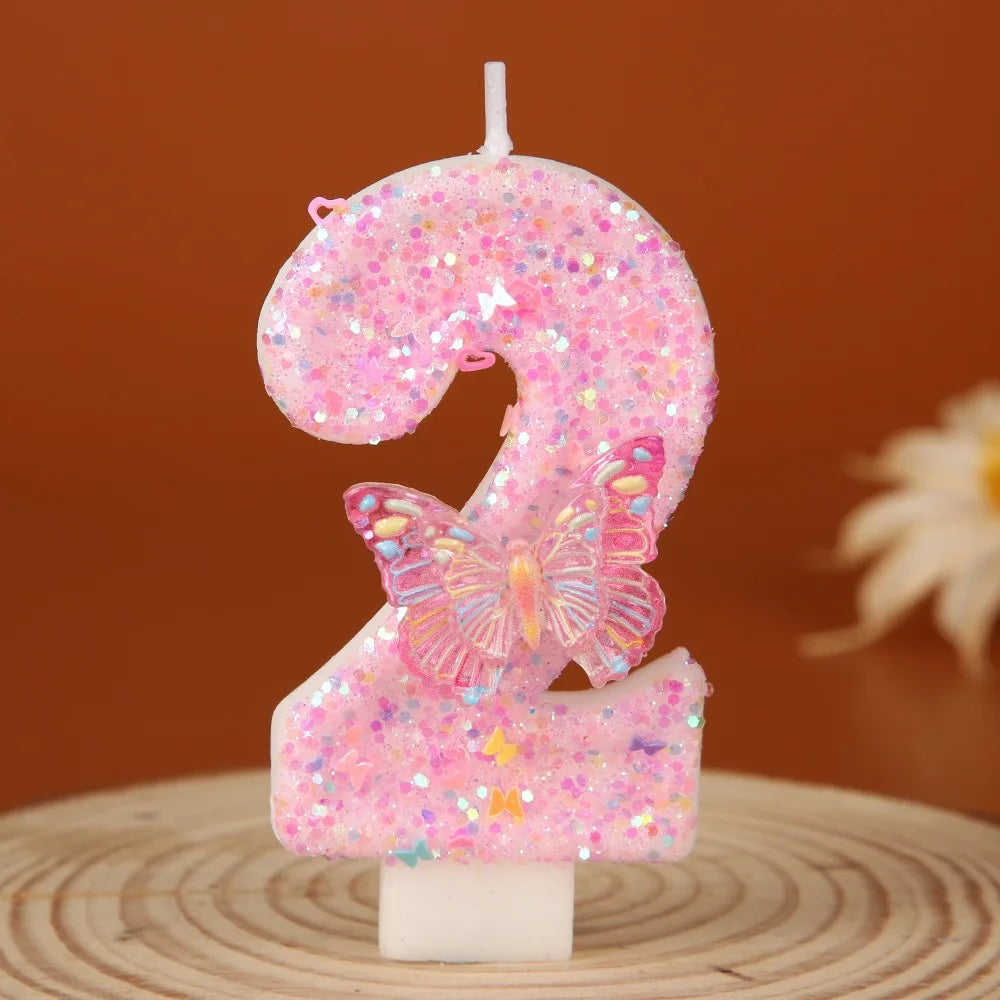 A pink glitter birthday candle shaped like the number 2 with a butterfly detail.