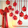 A set of ten round red foil balloons with ribbons hanging vertically against a white wall.