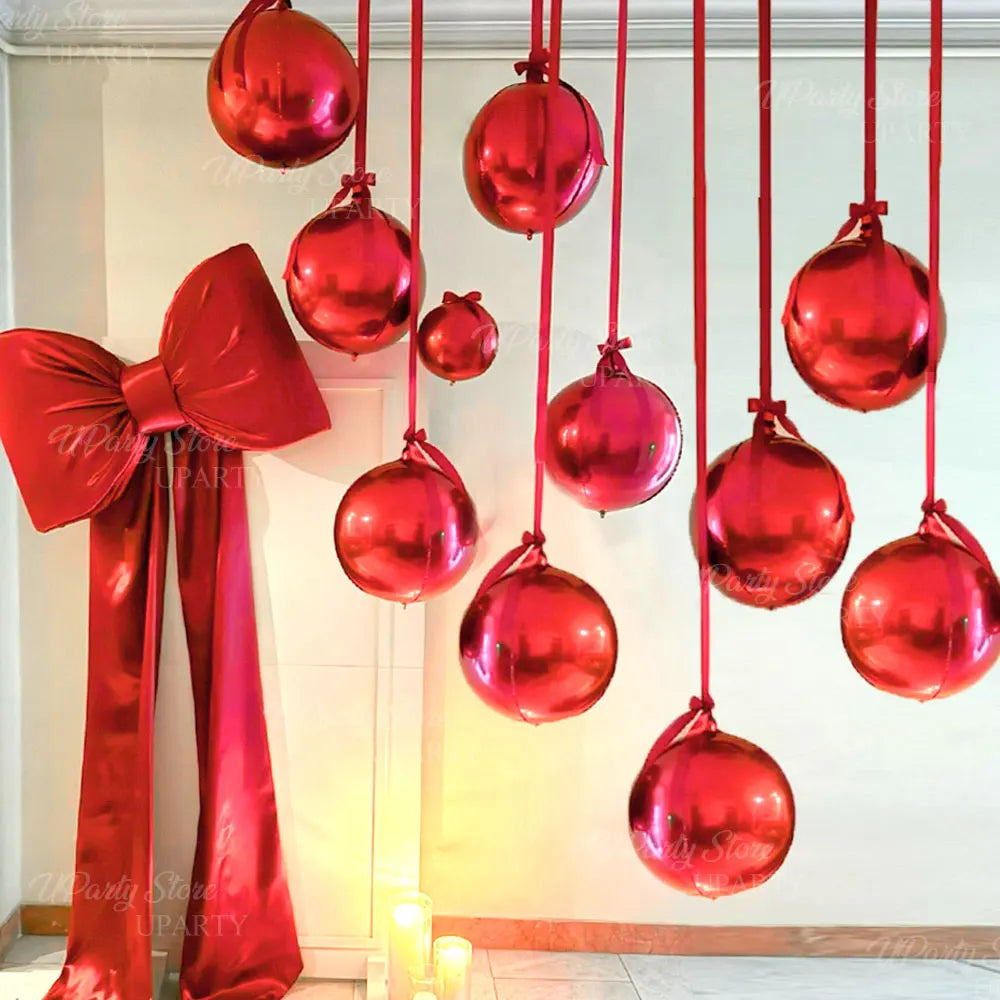 A set of ten round red foil balloons with ribbons hanging vertically against a white wall.