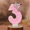 Pink glitter number three candle with a silver crown topper on a wooden base