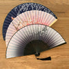 A vintage silk folding fan featuring delicate floral patterns in shades of pink, white, and dark blue.