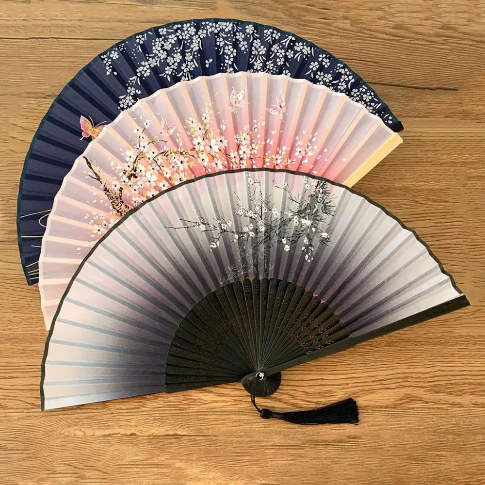 A vintage silk folding fan featuring delicate floral patterns in shades of pink, white, and dark blue.