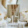 Elegant gold plated mirrored acrylic table numbers displayed with white flowers on a table.