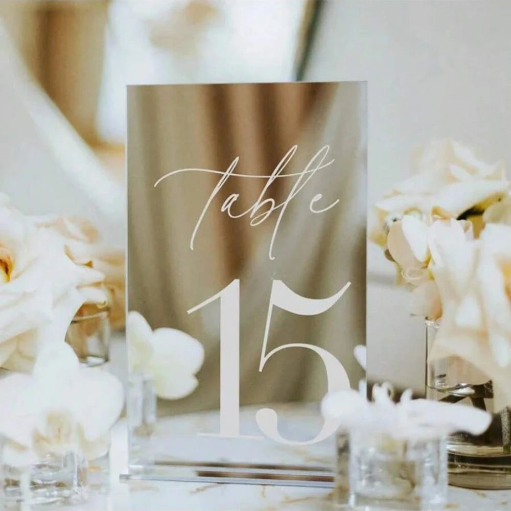 Elegant gold plated mirrored acrylic table numbers displayed with white flowers on a table.