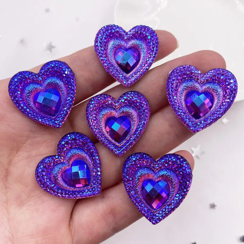 A hand holds a set of twelve heart-shaped purple iridescent resin rhinestone flatbacks.