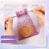 A purple organza drawstring bag decorated with gold stars and a slice of orange, being held by a hand.