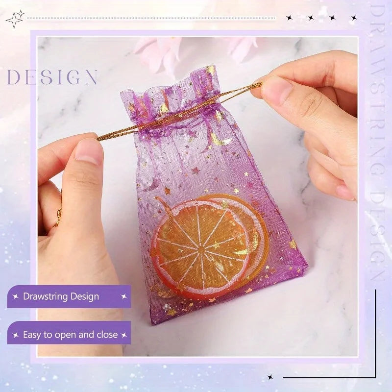 A purple organza drawstring bag decorated with gold stars and a slice of orange, being held by a hand.