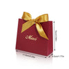 A red paperboard thank you gift bag tied with a gold ribbon.
