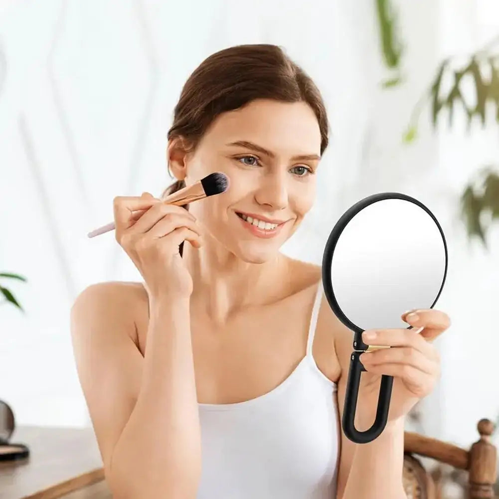 A woman applies makeup using a precision dual-magnification handheld mirror.