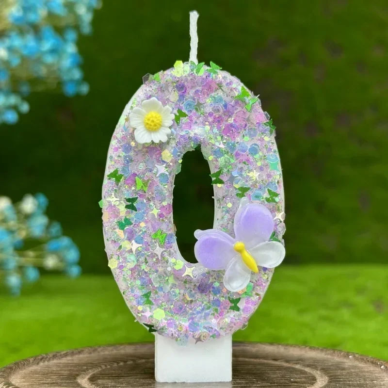 A purple and white number zero cake candle decorated with small flowers and a large lavender butterfly in an outdoor setting.