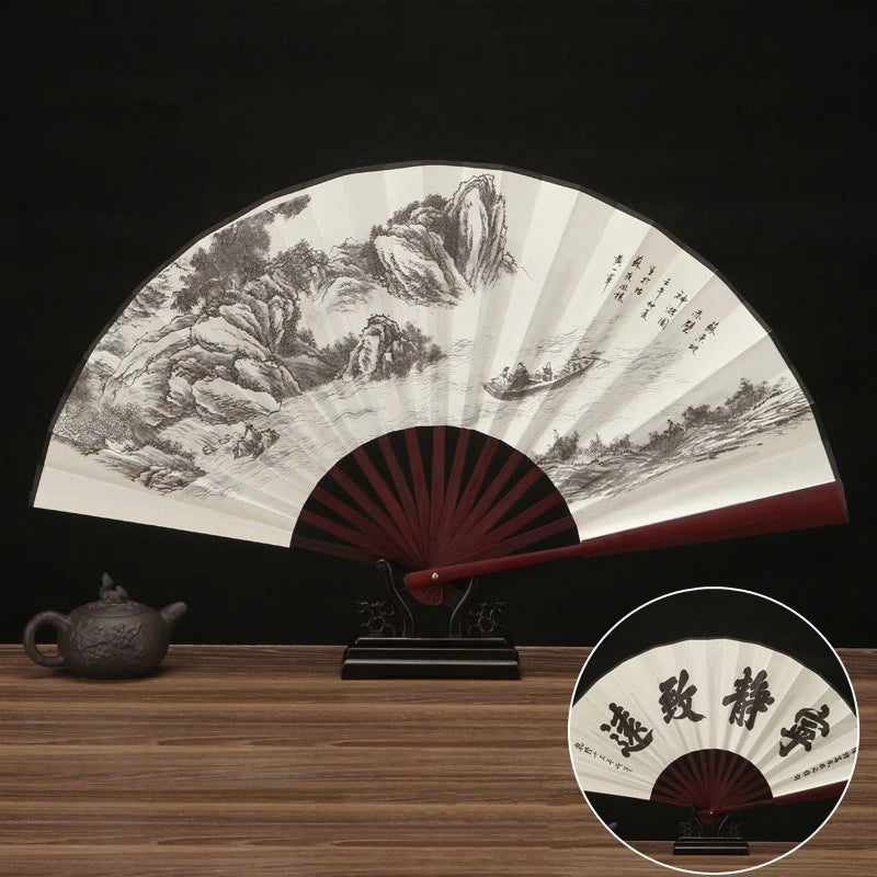 A large, folding silk and bamboo decorative fan displaying a detailed landscape painting in black and white.