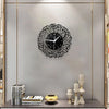 A black acrylic wall clock with intricate Arabic calligraphy design mounted on a gray wall.