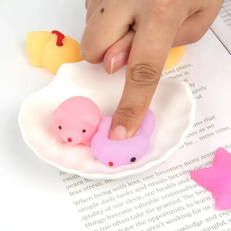 A hand is placing a pink, round cartoon animal stress relief toy onto a white ceramic dish.