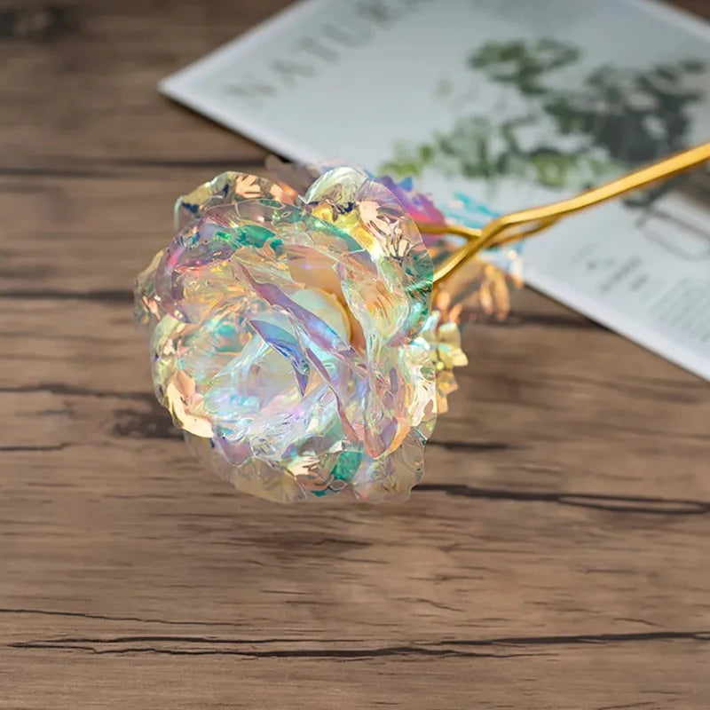A close-up of rainbow artificial crystal flowers attached to a gold wire, resting on a wooden surface.