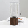 A tall, clear glass vase with a dark wooden base is shown standing upright on a white surface.