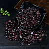 A pile of deep burgundy garnet crystal chips is displayed in a black dish on a dark surface.