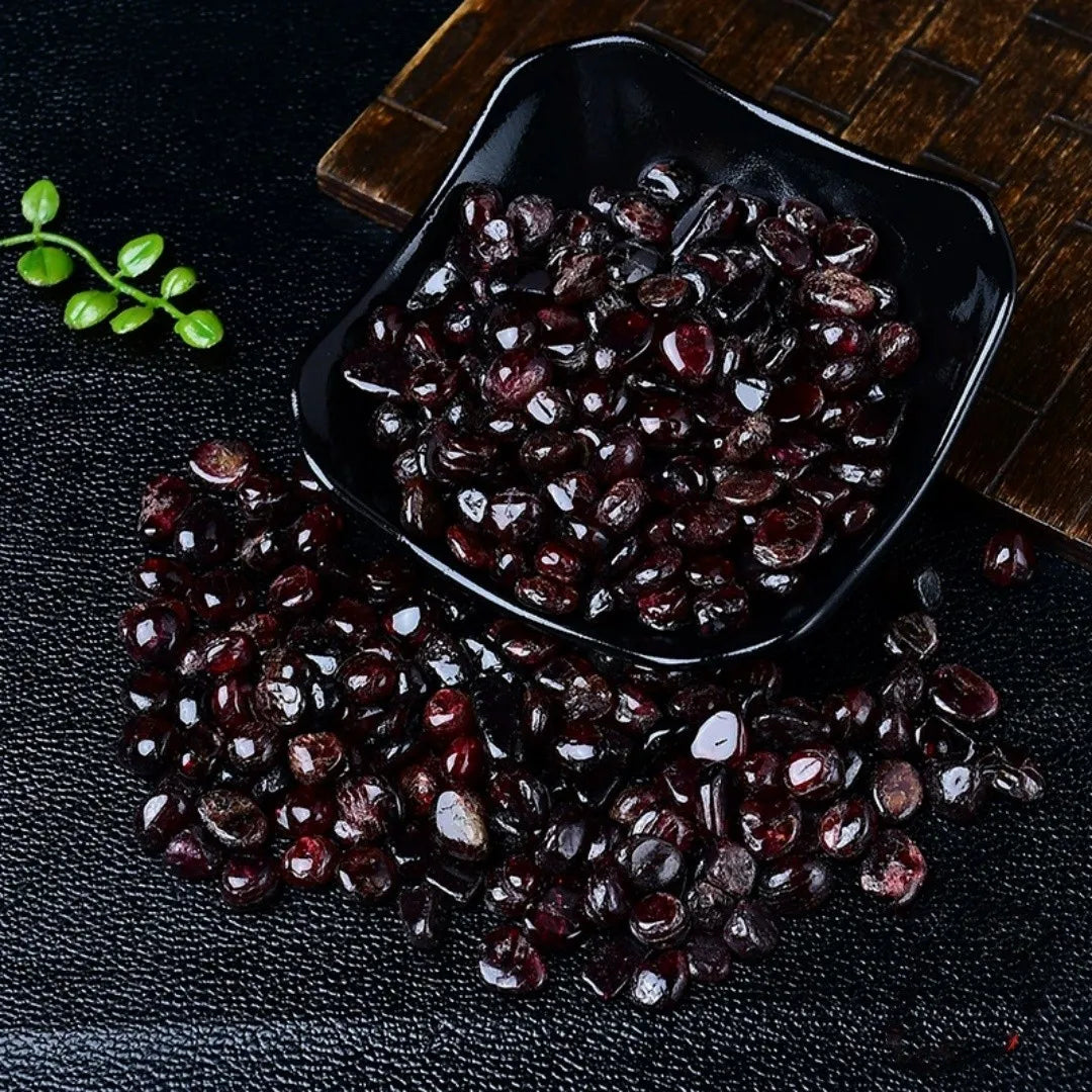 A pile of deep burgundy garnet crystal chips is displayed in a black dish on a dark surface.