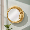 A round, gold resin decorative hanging mirror shaped like a crescent moon is mounted on a light-colored wall.
